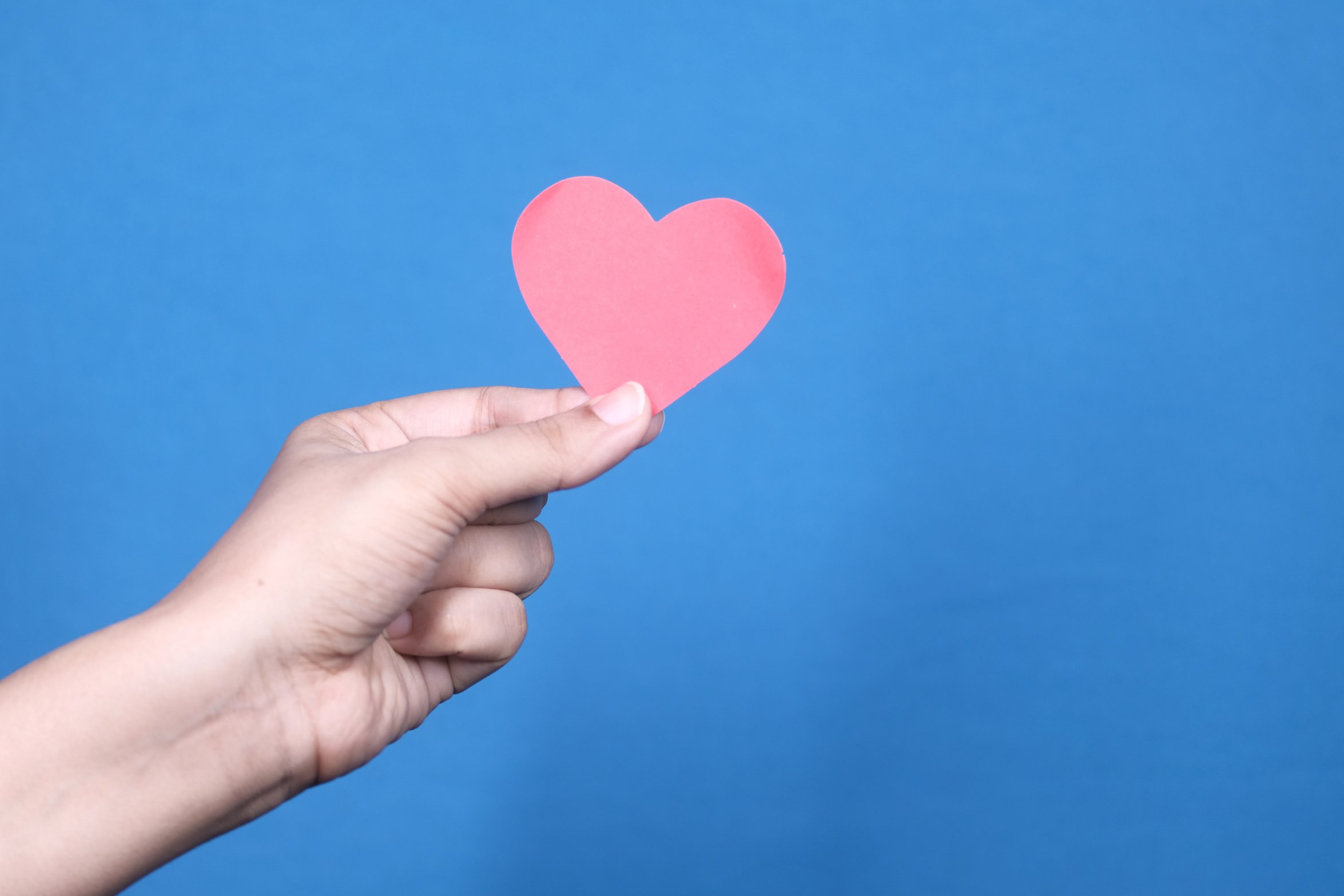 Hand Holding Red Heart with Copy Space against Blue Background